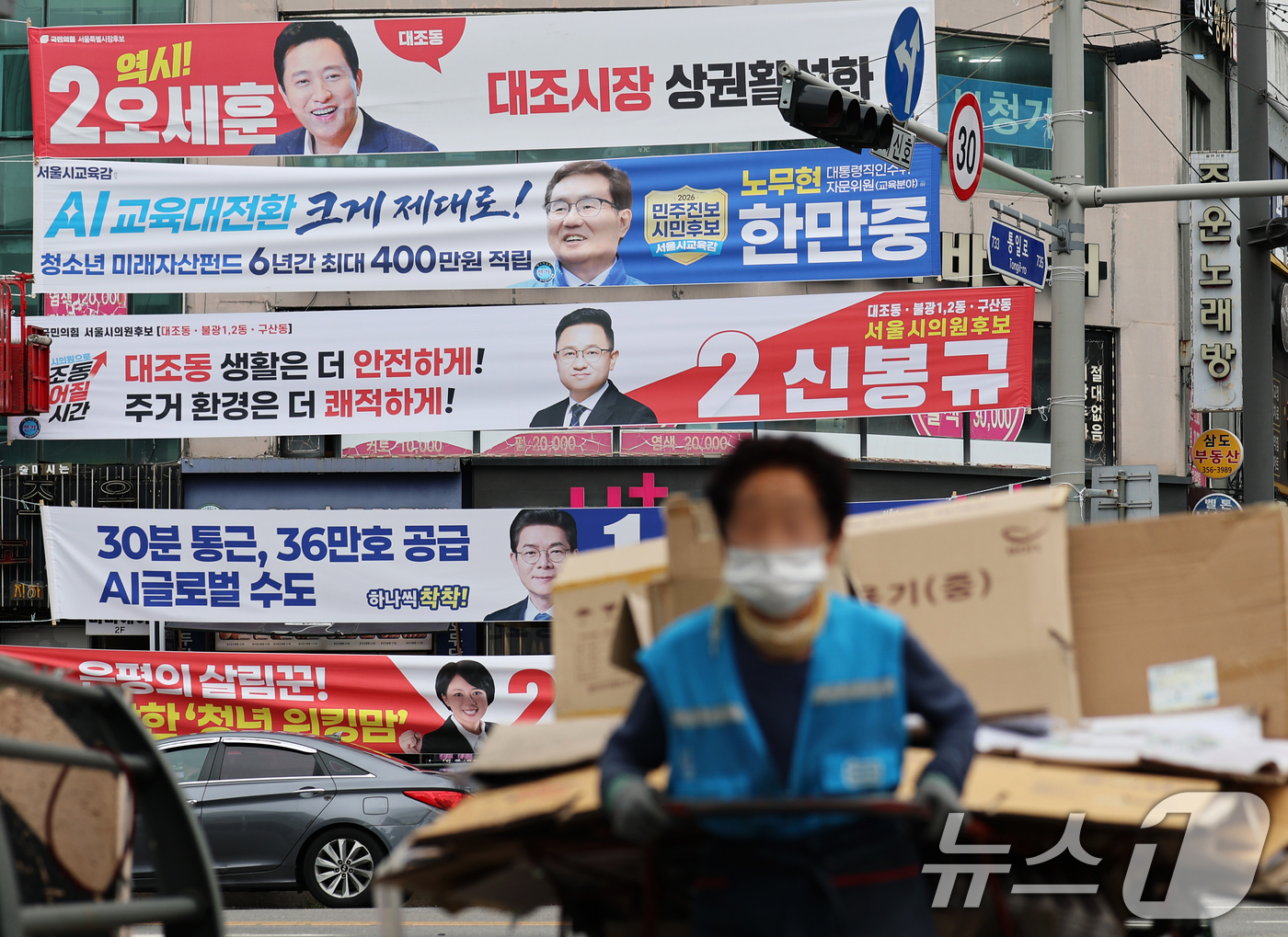 (서울=뉴스1) 오대일 기자 = 6·3 지방선거 공식 선거운동이 시작된 21일 서울 은평구의 한 거리에서 폐지 수레를 끄는 할머니가 여야 후보자들의 선거 현수막 앞을 힘겹게 지나고 …