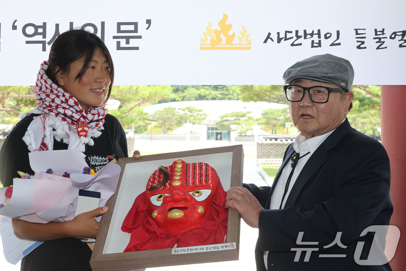 (광주=뉴스1) 박지현 기자 = 23일 오전 광주 북구 운정동에 위치한 국립 5·18민주묘지 역사의문 앞에서 김아현 씨(활동명 해초)가 봉산탈춤의 탈을 선물받고 있다. 김 활동가는 …
