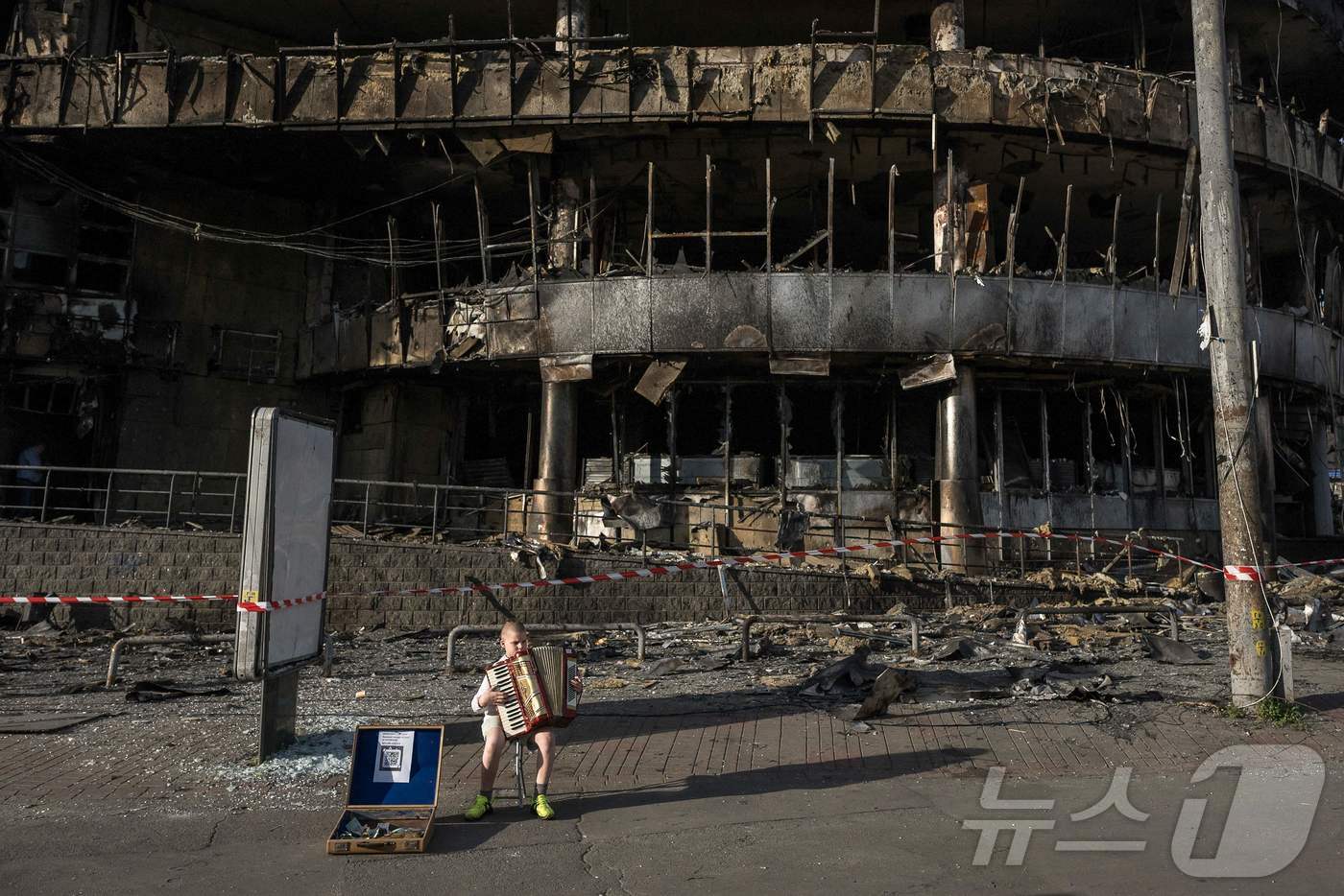(키이우 AFP=뉴스1) 김경민 기자 = 러시아의 우크라이나 공습으로 피해를 본 키이우 한 쇼핑센터 앞에서 소년이 25일(현지시간) 아코디언을 연주하고 있다. 2026.5.25ⓒ …