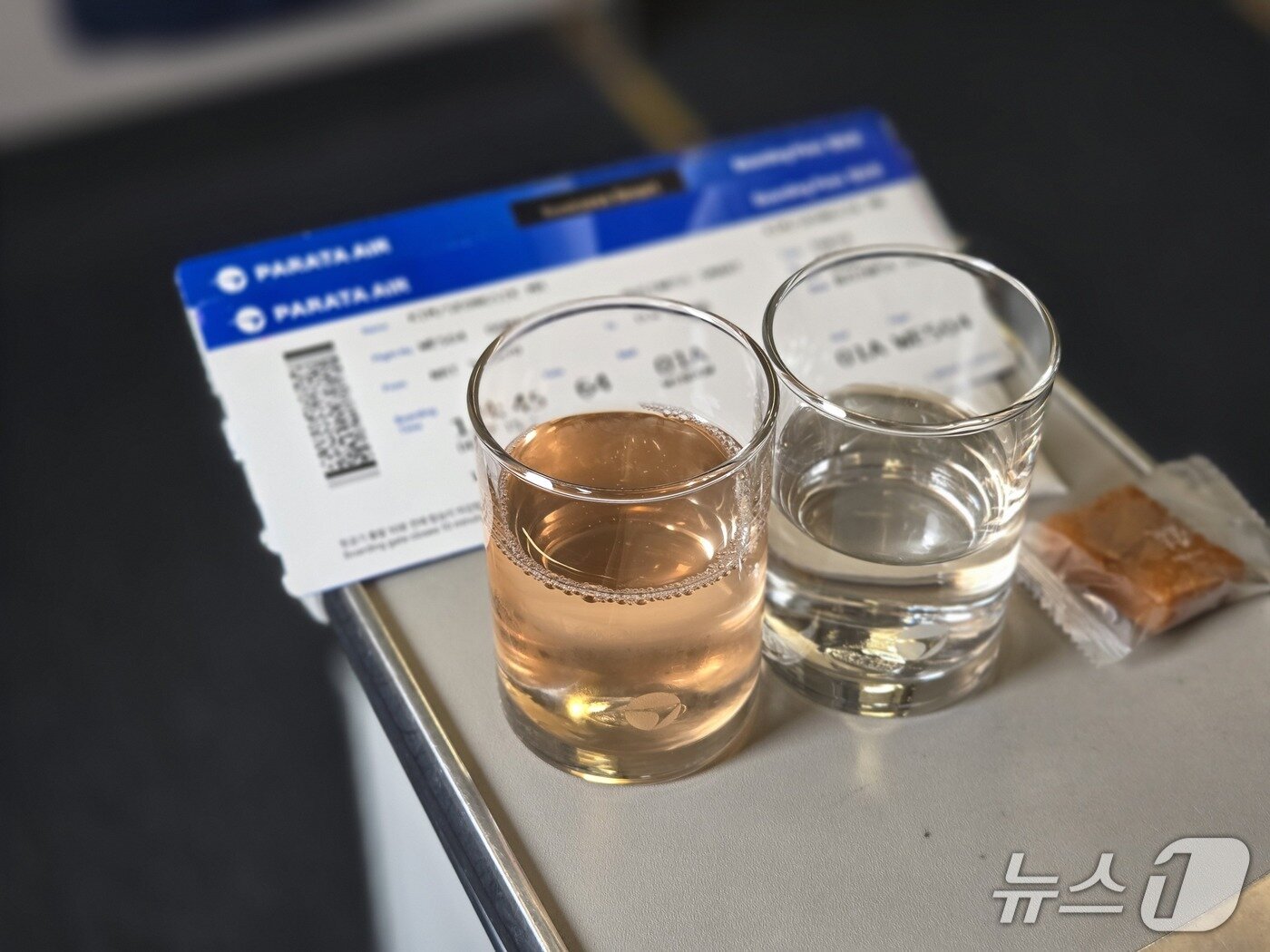 본문 이미지 - 6일 인천을 출발해 도쿄로 향하는 파라타항공 A330-200 항공기 비즈니스 스마트석에서 웰컴 드링크로 파라타항공의 시그니처 음료인 '피치 온 보드'(왼쪽)와 물(오른쪽)을 약과와 함께 제공받은 모습. 피치 온 보드는 복숭아와 포도맛이 났다. 2025.5.6/뉴스1 김성식 기자