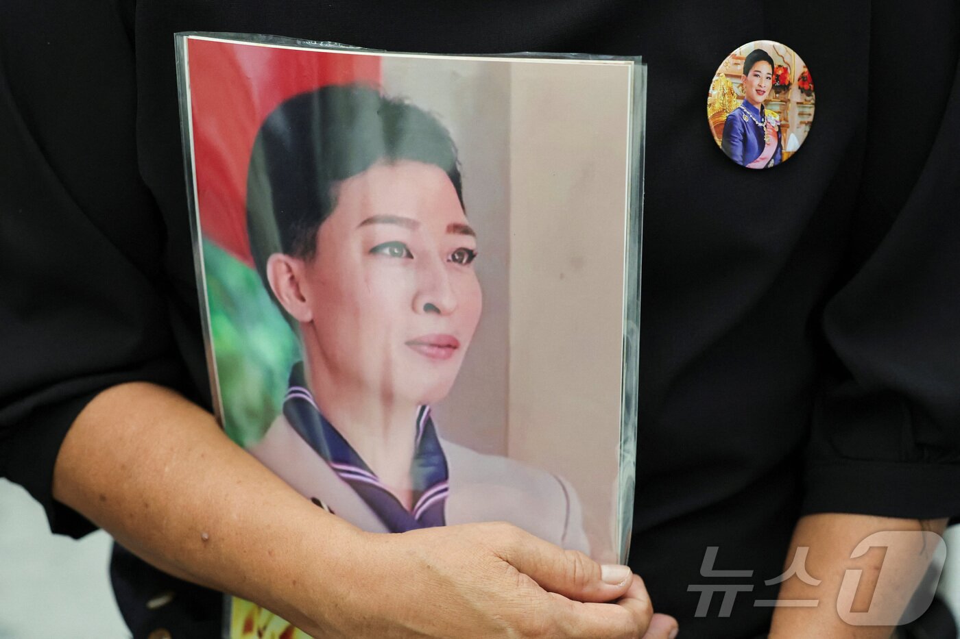 본문 이미지 - 12일(현지시간) 태국 방콕의 쭐랄롱꼰 기념 병원 밖에서 한 사람이 이날 사망한 랏차사리니시리팟 공여 파차라키티야파 공주의 사진을 들고 그의 모습이 담긴 배지를 달고 있다. 2026.06.12 ⓒ 로이터=뉴스1
