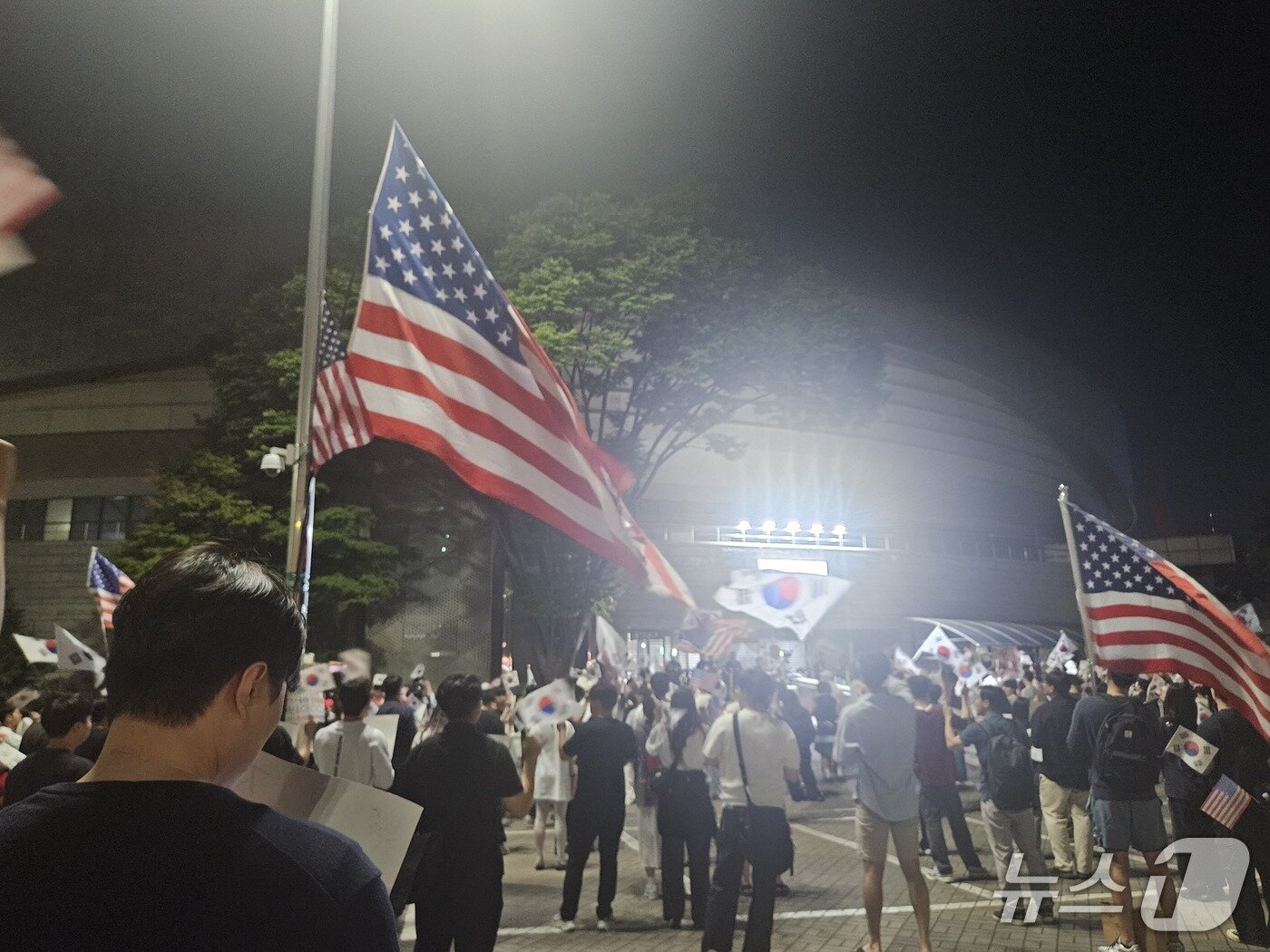 본문 이미지 - 제9회 전국동시지방선거 투표용지 부족 사태에 반발한 시민들이 12일 오후 10시 서울 송파구 올림픽공원 핸드볼경기장을 봉쇄하며 시위를 하는 가운데 대형 성조기가 내걸린 모습. 2026.6.12 ⓒ 뉴스1 유채연 기자
