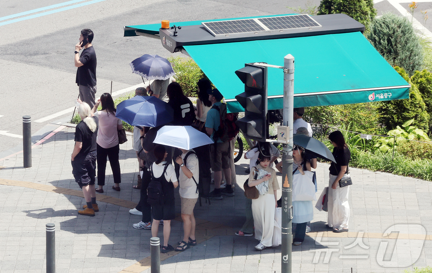 (서울=뉴스1) 김진환 기자 = 낮 최고 기온이 30도 가까이 오르며 무더운 날씨를 보인 26일 서울 중구 을지로입구역 사거리에서 시민들이 횡단보도 앞 그늘막 아래 모여 신호를 기 …