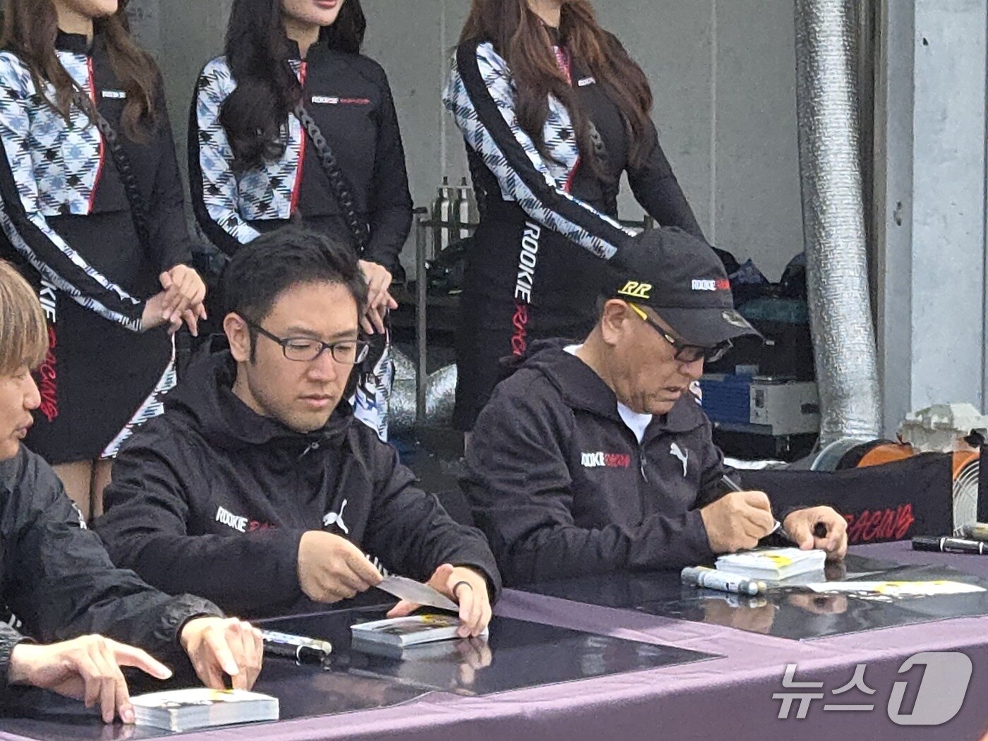 본문 이미지 - 6일 일본 시즈오카현 후지 스피드웨이에서 내구 레이스 대회 '슈퍼 타이큐 2026' 3라운드 개막을 기념해 도요다 아키오 도요타 회장이 속한 도요타 가주 루키 레이싱(TGRR)팀이 연 사인회에서 아키오 회장(오른쪽)과 그의 장남 도요다 다이스케 우븐 바이 도요타 수석 부사장이 사인을 하고 있다. 2026.6.6/뉴스1 김성식 기자