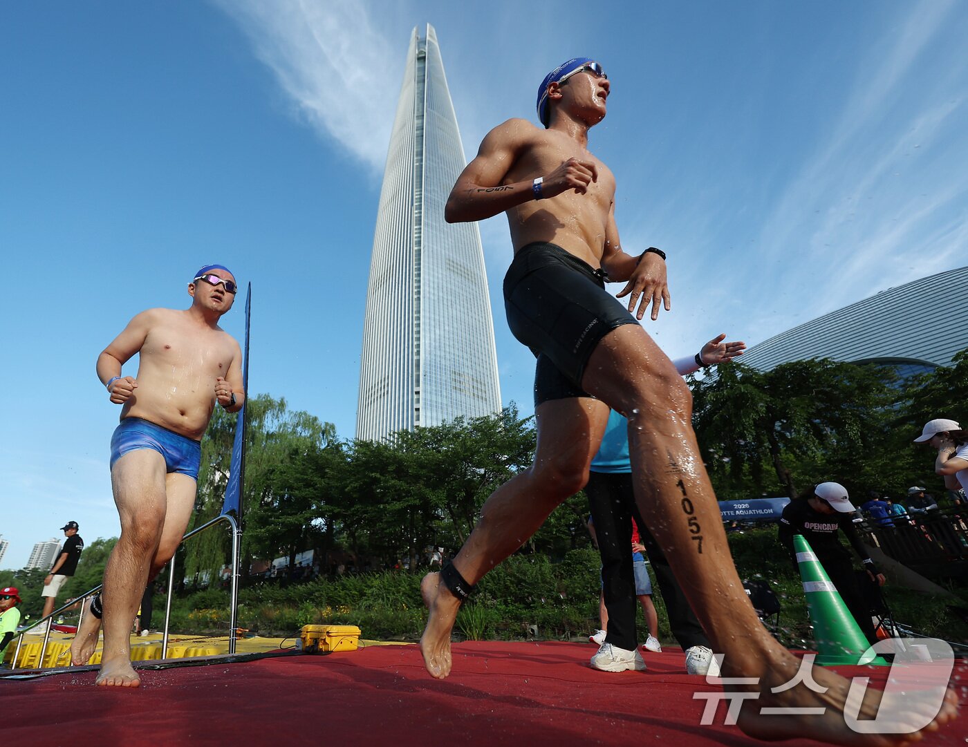 본문 이미지 - 12일 오전 서울 송파구 석촌호수와 롯데월드타워 일원에서 열린 '2026 롯데 아쿠아슬론'에서 수영을 마친 참가자들이 수직마라톤을 위해 롯데월드타워로 향해 달리고 있다. (공동취재) 2026.7.12 ⓒ 뉴스1 구윤성 기자