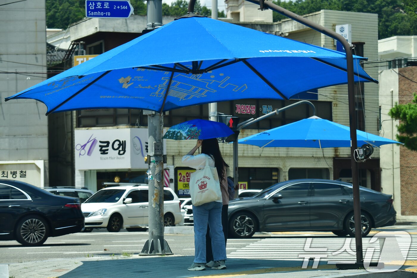 본문 이미지 - 경북 포항시 전역에 폭염 중대경보가 발령된 12일 포항시 북구에서 시민들이 육거리 횡단보도에 설치된 대형 우산 그늘막 아래에서 신호를 기다리고 있다. 포항시는 폭염 중대경보가 발령되지 재난 상황 2단계를 발령하고 재난부서 및 필수인력에 대한 비상근무를 명령했다. 2026.7.12 ⓒ 뉴스1 최창호 기자