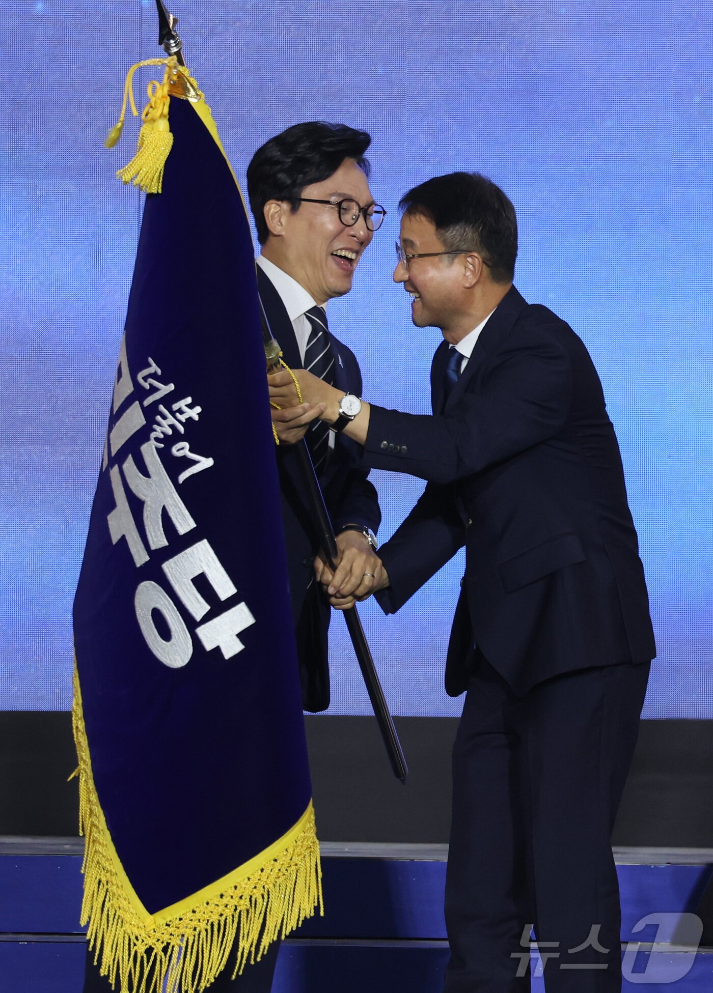 본문 이미지 - 더불어민주당 김민석 신임 당대표가 17일 대전시 유성구 대전컨벤션센터에서 열린 더불어민주당 제3차 정기전국당원대회에서 한병도 원내대표로부터 당기를 건네받고 있다. (공동취재) 2026.8.17 ⓒ 뉴스1 황기선 기자