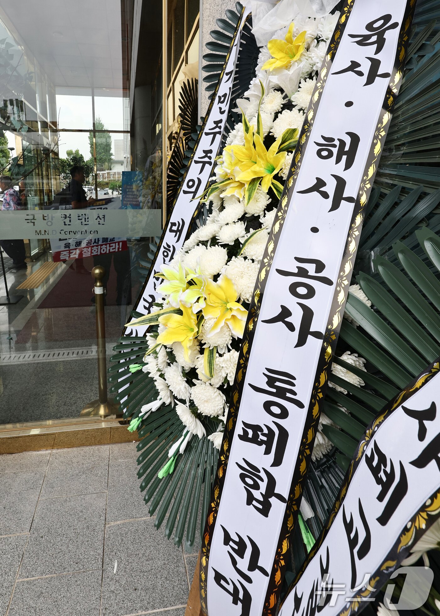 본문 이미지 - 26일 오후 국군사관학교 창설 공청회가 열린 서울 용산구 국방컨벤션 앞에 국군사관학교 창설 반대 화환이 설치되어 있다. 2026.8.26 ⓒ 뉴스1 최지환 기자