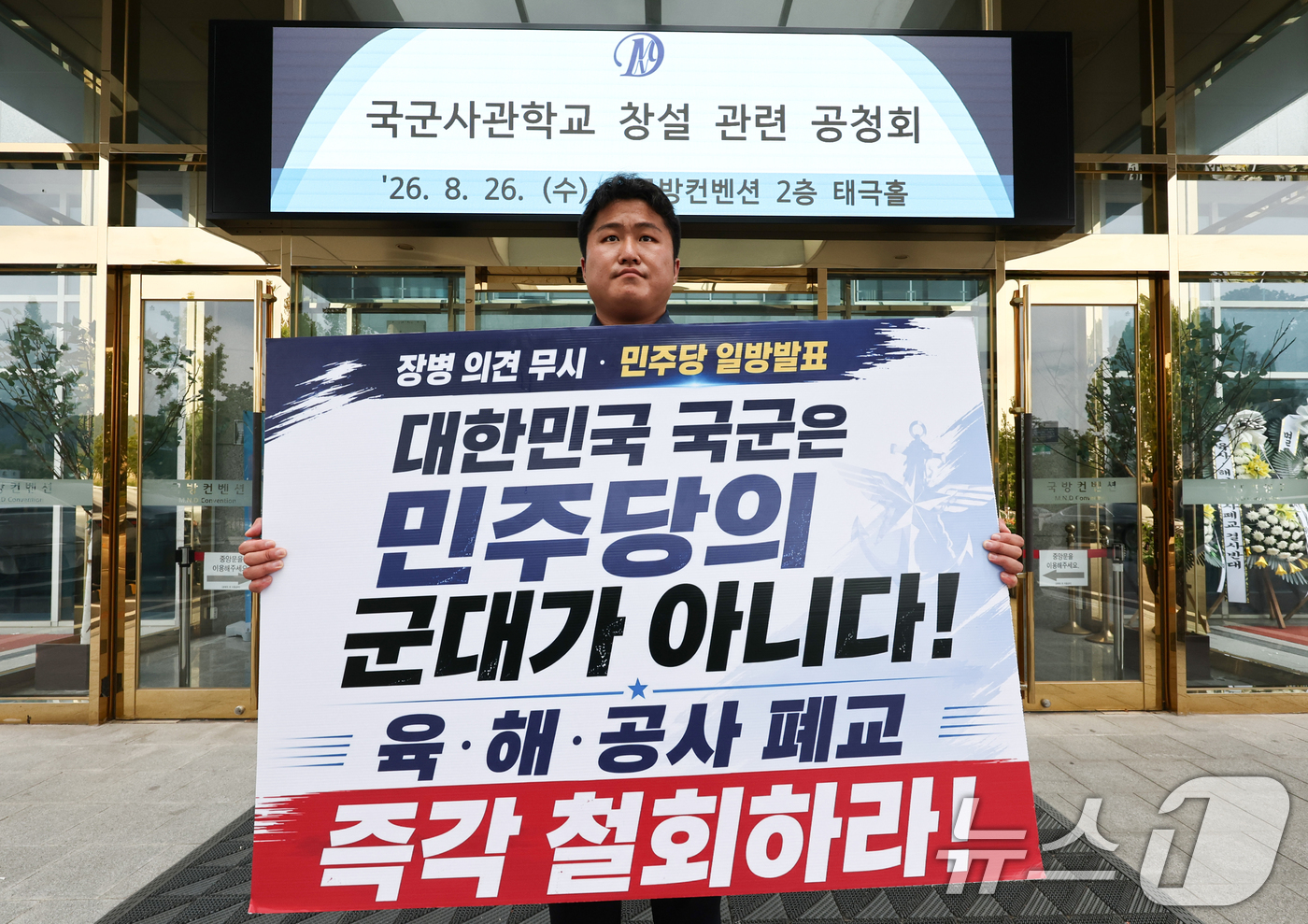 (서울=뉴스1) 최지환 기자 = 26일 오후 국군사관학교 창설 공청회가 열린 서울 용산구 국방컨벤션 앞에서 한 시민이 사관학교 통합 반대 1인 시위를 하고 있다. 2026.8.26 …