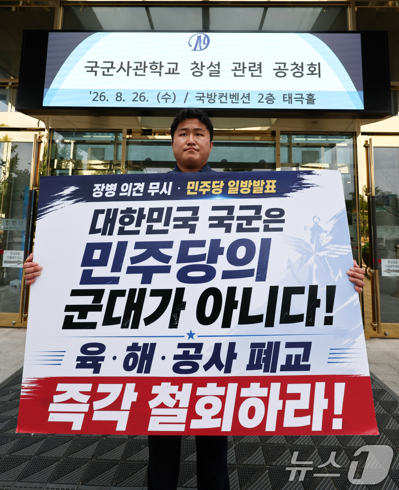 (서울=뉴스1) 최지환 기자 = 26일 오후 국군사관학교 창설 공청회가 열린 서울 용산구 국방컨벤션 앞에서 한 시민이 사관학교 통합 반대 1인 시위를 하고 있다. 2026.8.26 …