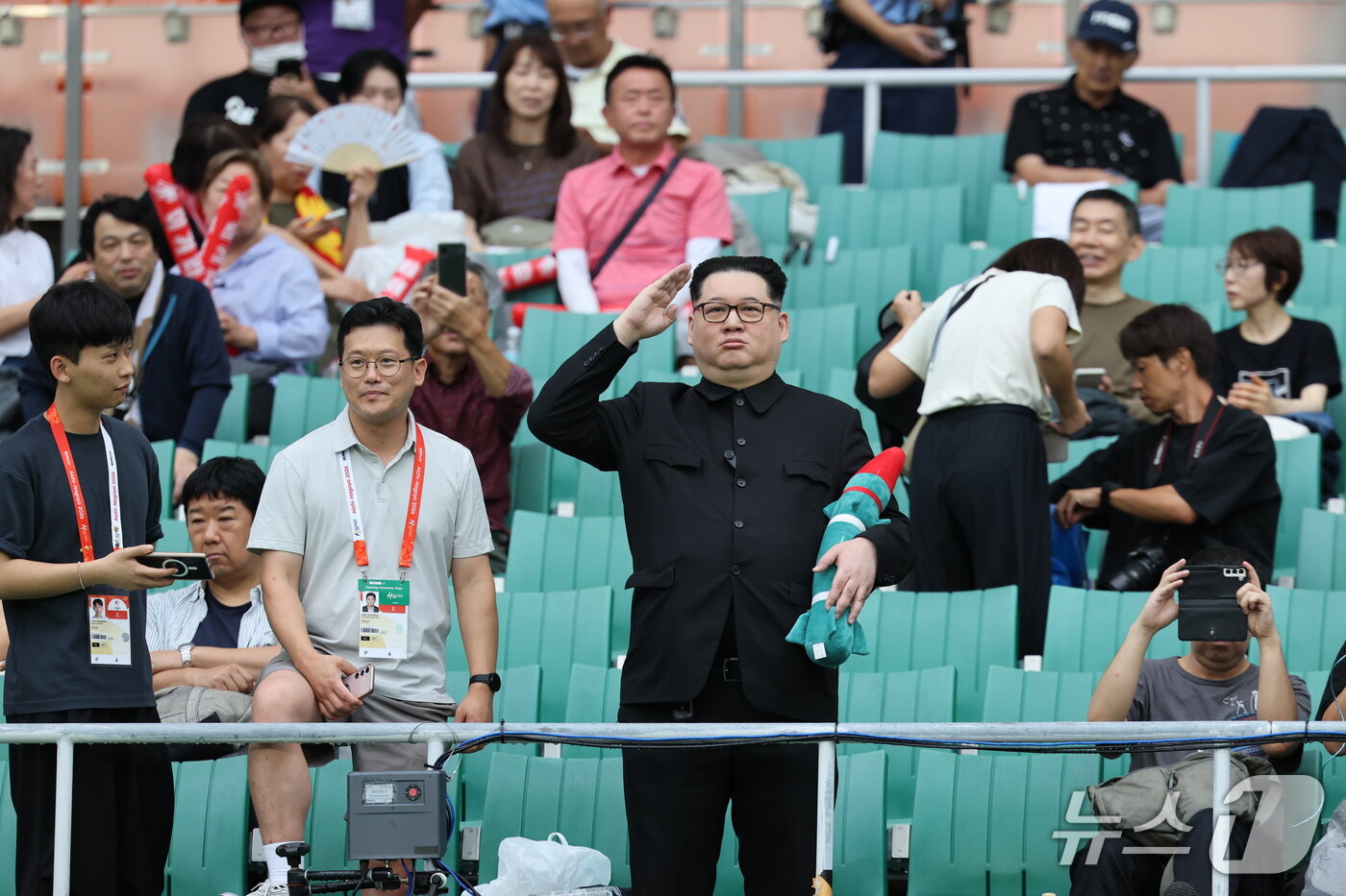 본문 이미지 - 21일 일본 시즈오카 스타디움 에코파에서 열린 2026 아이치·나고야 아시안게임 조별예선 F조 대한민국과 북한의 경기에 북한 김정은 국무위원장 모습으로 나타난 중국계 정치활동가 '하워드X'가 경례를 하고 있다. 2026.9.21 ⓒ 뉴스1 안은나 기자