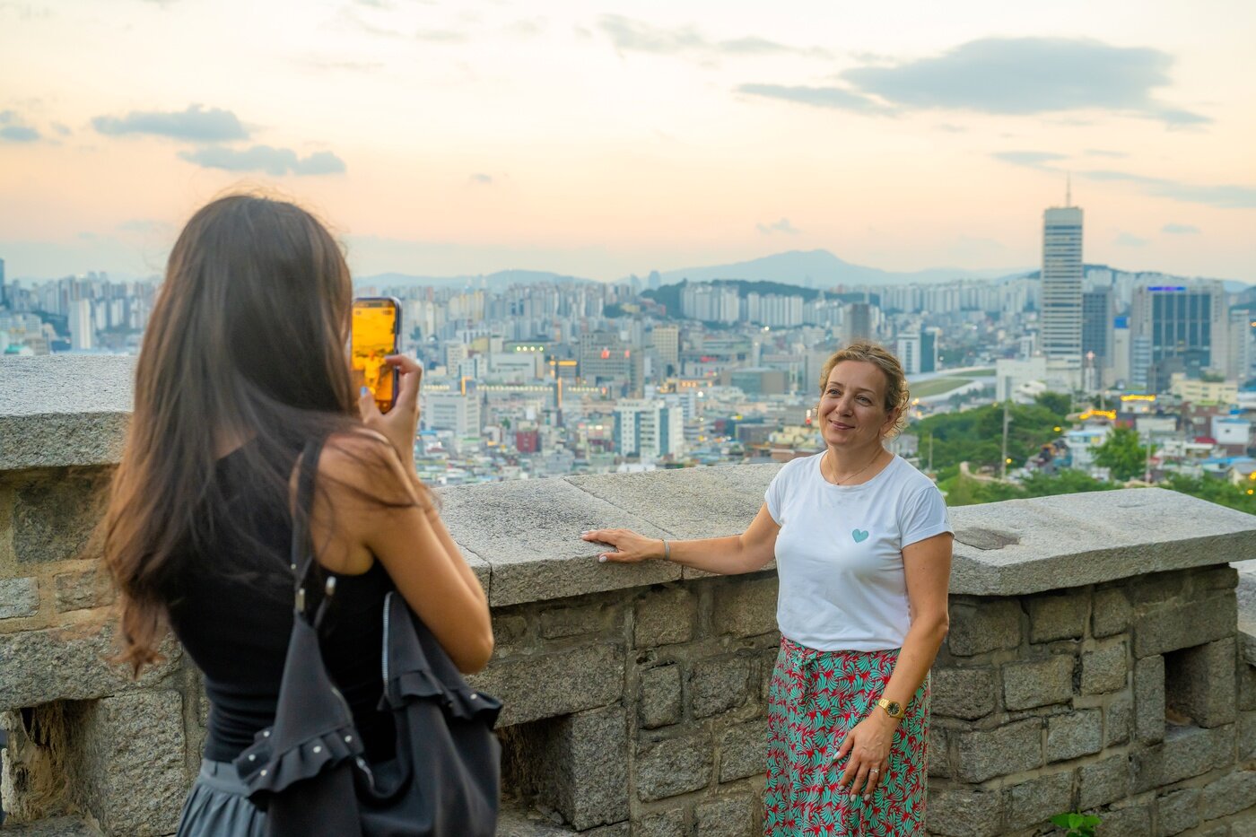 본문 이미지 - 낙산에서 성곽과 도심을 배경으로 촬영하는 여행객(서울관광재단 제공)